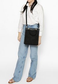 Borsa nera con texture, dotata di doppi manici superiori e una lunga tracolla regolabile. Presenta dettagli in ottone e una forma rettangolare strutturata.