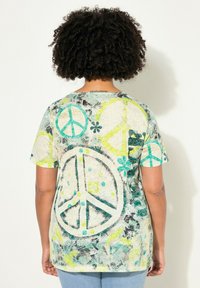 Camisa de manga corta con un estampado de símbolo de paz multicolor, principalmente en aqua y amarillo, sobre un fondo claro con un diseño texturizado.