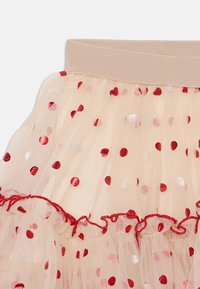jupe en tulle superposée de couleur rose pâle avec des pois rouges et argentés. Dotée d'une large taille élastique et d'un ourlet à volants.