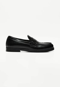Black leather loafers with a flat sole, featuring a stitched detail and a decorative strap across the front. Smooth finish, classic design.