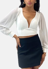 Haut court blanc avec un décolleté en V profond et des manches longues transparentes, associé à une mini-jupe noire ajustée. Tissu lisse avec une silhouette épurée.