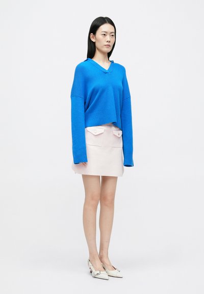 Niebieski krótkowłosy sweter z dekoltem w serek i długimi rękawami, w zestawieniu z jasnoróżową mini spódnicą z dwoma kieszeniami z przodu. Białe szpiczaste buty.