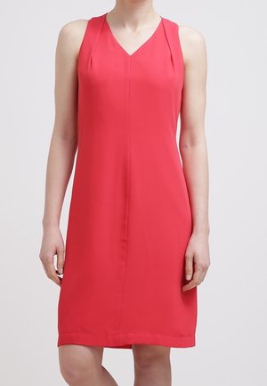 Robe rouge sans manches longueur genou avec décolleté en V portée par une personne debout sur un fond blanc uni.