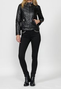 Giacca di pelle nera trapuntata con colletto alto, tasche con zip e dettagli. Abbinata a jeans skinny neri e stivaletti.