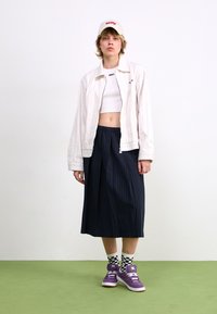 Hvitstripet jakke over en hvit crop top, kombinert med et marineblått pinstripe-skjørt. Lilla sneakers med hvite lisser og rutete sokker.