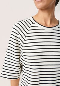 T-shirt a righe bianche e nere, realizzato in cotone morbido, con collo rotondo e maniche corte raglan. Presenta un motivo a righe orizzontali.