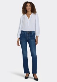 Blusa blanca de manga larga con escote en ojal, combinada con vaqueros azul oscuro de pierna recta, con bolsillos delanteros y costuras visibles.