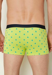 Grüne Boxershorts mit einem blauen Apfelmuster, versehen mit einem marineblauen Bund. Hergestellt aus einem glatten, dehnbaren Stoff für zusätzlichen Komfort.
