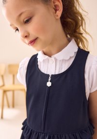 Tumesinine kleit volangilise äärega ja luku sulgumisega, millel on lilleline tõmblukukäepide. Kihiline üleval valge kraega särgiga.