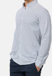 Košile s dlouhým rukávem na knoflíky v světle modré barvě s geometrickým vzorem. Má límec, bílé knoflíky a pohodlný střih.