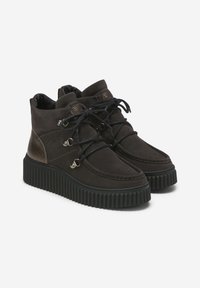 Stivali alla caviglia in suede marrone con suola nera spessa, dotati di hardware in metallo, lacci e una finitura liscia sul tallone.