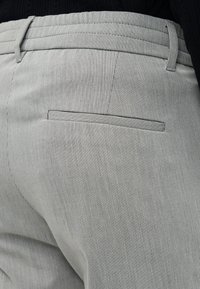 Primer plano de pantalones gris con rayas finas, con bolsillo de ojal trasero y trabillas para cinturón, combinados con una camiseta negra metida por dentro.