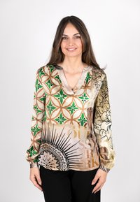 Seidenbluse mit einem mehrfarbigen geometrischen Muster und grünen Akzenten, beigem Grund, V-Ausschnitt und langen Ärmeln. Text- und Blütendetails enthalten.