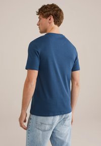 Tamsiai mėlynas apvalios iškirptės marškinėliai, trumpomis rankovėmis, minkšta tekstūra, aptemptas dizainas, dėvimi su šviesiai mėlynomis džinsinėmis kelnėmis, vaizdas iš nugaros.