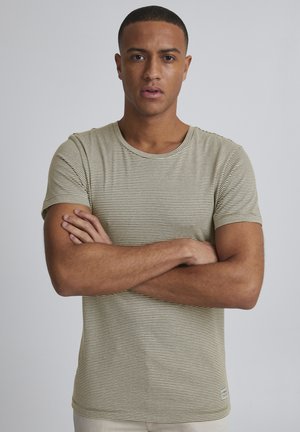 Striped short-sleeve t-shirt in light olive and cream, featuring a rounded neckline and a small branded tag at the hem. Smooth fabric texture.