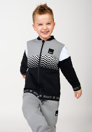 Giacca nera e grigia con zip e design a scacchi. Pantaloni della tuta grigio chiaro con una cintura con logo nera.
