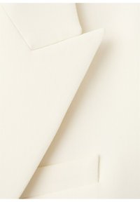 Off-white habitjakke med reversflip og en matchende lommetørklæde af samme stof, der er stukket ned i brystlommen.