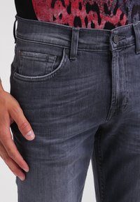 Jeans de mezclilla gris oscuro con un diseño clásico de cinco bolsillos, costuras visibles y corte recto. La tela tiene un ligero desgaste y una textura suave.