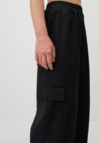 Zwarte, loszittende cargobroeken met een elastische tailleband, textuurstof en een zijzakdetail.