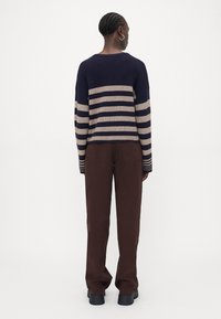 Marineblå og beige stripete genser med lange ermer, ribbet tekstur, rund hals, parret med brune vide bukser og svarte kraftige sko.