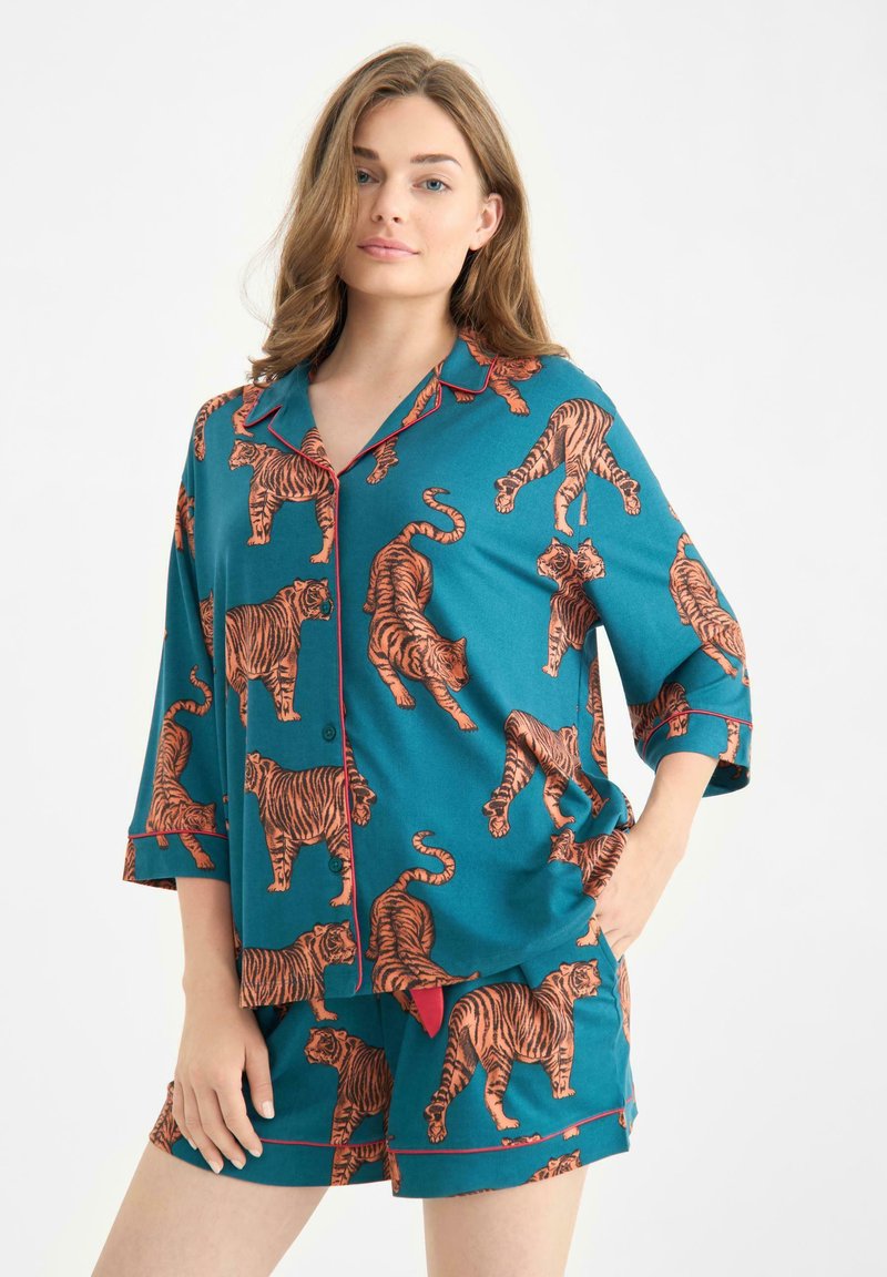 Conjunto de pijama turquesa con un estampado de tigres naranjas por todas partes. Camiseta de manga corta con cuello y ribete rojo, acompañada de pantalones cortos a juego.