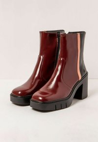 Botines de charol burdeos con una franja de acento negra y rosa, tacón robusto y suela negra estriada, con cremallera lateral.