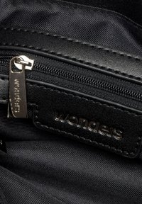 Acercamiento a la cremallera de una bolsa de tela negra y cuero con un tirador metálico y la etiqueta de la marca "wonders" grabada.