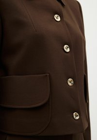 Brun skræddersyet jakke med en glat tekstur, store forlommer og metalliske knapper. Det enkle kravedesign fremhæver det strukturerede look.