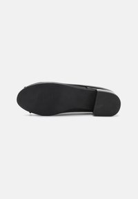 Black flat shoe with a smooth leather upper, rounded toe, and a textured rubber sole. Design focuses on minimalism and streamlined shape.