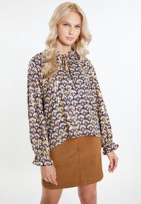 Blusa multicolore a fantasia con maniche a sbuffo e collo a cravatta. Abbinata a una mini gonna in suede marrone.