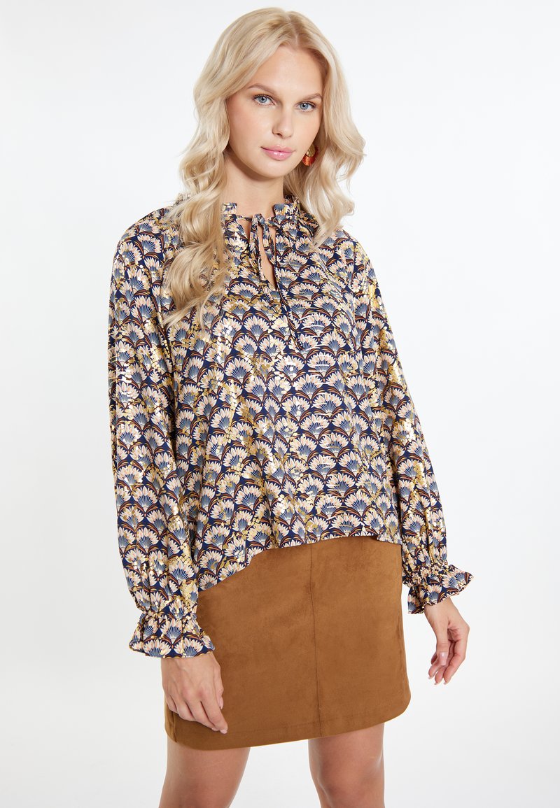 Blusa multicolore a fantasia con maniche a sbuffo e collo a cravatta. Abbinata a una mini gonna in suede marrone.