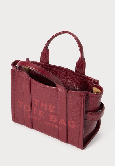 Burgundy leather tote bag with a structured design, featuring two short handles, embossed text, and a smooth texture.