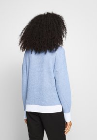 Ljust blå stickad tröja med rund halsringning, texturerat mönster och vit ribbad fåll och muddar. Avslappnad passform, lång ärm och sidoflikar.