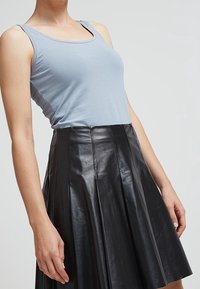 Light blue tank top made of soft fabric paired with a black pleated leather skirt featuring visible seams and a flared design.