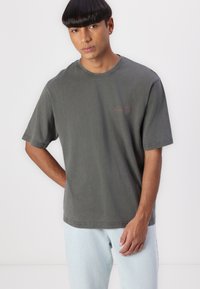 Gray cotton t-shirt with short sleeves, featuring a round neckline and subtle logo in red. Paired with light blue denim pants.