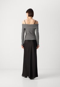 Haut noir à épaules dénudées avec des rayures blanches verticales, associé à une longue jupe noire. Tissu lisse et design ajusté.