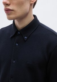 Tengerészkék póló texturált anyagból, gombos gallérral, apró díszgombokkal és finoman hímzett "BOSS" logóval.