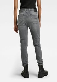 Jeans skinny grises con una cintura alta, con bolsillos traseros y una textura suave. Combinados con botas negras hasta el tobillo.