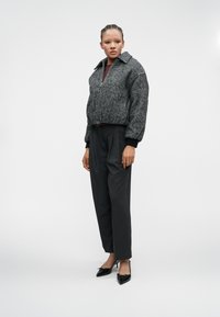 Veste cropped à motif pied-de-poule gris avec col, associée à un pantalon sombre ajusté et des escarpins noirs à bout pointu. Tissu lisse et design structuré.