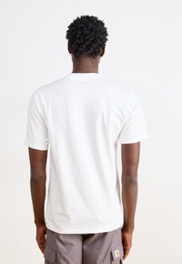 T-shirt bianca in cotone con maniche corte, scollatura rotonda e una texture liscia, indossata con pantaloni cargo grigi. Nessun motivo o dettaglio degno di nota.