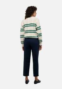 Pull en tricot de couleur crème avec des rayures vertes et bleu foncé, à manches courtes et bords côtelés ; associé à un pantalon bleu marine et des ballerines noires.