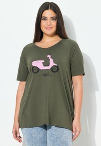 Camiseta verde oliva de manga corta, con un gráfico de un patinete rosa y el texto "1987". Tela suave y corte relajado.