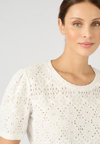 Witte top met korte mouwen, kenmerken een getextureerd, geborduurd patroon met ruitvormen en uitsparingen. Ronde halslijn met een zachte afwerking.