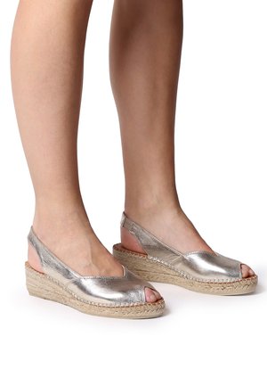 Metallic silver espadrille wedges with open toe and slingback design. Jute rope midsole adds texture. Smooth leather upper with stitching details.