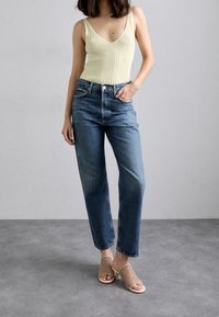 Top sin mangas amarillo claro con textura acanalada, vaqueros azules de talle alto y sandalias deslizantes beige de tejido trenzado. Diseño sencillo con colores neutros y corte relajado.