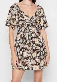 Blumenkleid mit kurzen, gerafften Ärmeln. Schwarzer Hintergrund mit weißen, gelben und rosa Blumen. Betonter Taillenbereich, ausgestellter Rock, glatte Stoffstruktur.