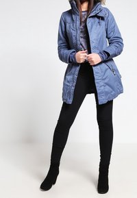 Blå vadderad jacka med dragkedja och tryckknappsstängning, justerbar huva, texturerade axlar och två sidofickor med dragkedja.