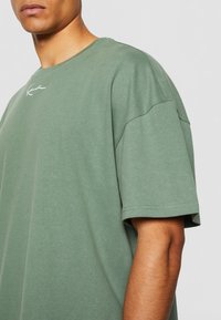 Grønn bomulls t-skjorte med rund hals, korte ermer og en subtil brodert logo på brystet. Glatt tekstur og avslappet passform.