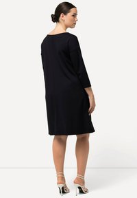 Abito nero al ginocchio con maniche a tre quarti, scollatura rotonda e vestibilità rilassata. Tessuto liscio con una leggera texture. Sandali con tacco.