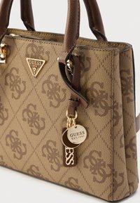 Ruda tekstūruota rankinė su deimanto raštu, su auksiniu logotipo plokštelės, odiniais rankenomis ir dekoratyvinėmis metalinėmis etiketėmis.